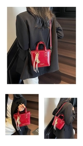 Detail view of red glossy patent leather handbag with woven tassel and crossbody strap