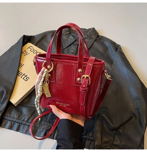 Close-up of red patent leather bucket bag with gold lettering and woven charm detail