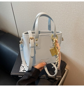 Detail of light blue bucket bag with gold charms and branded logo text on textured leather