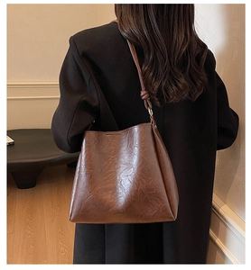 Detail of dark brown leather bucket bag with knotted strap and embossed logo texture