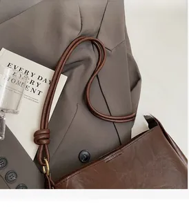 Close-up of dark brown leather bucket bag featuring knot handle and gold hardware detail