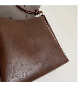Detail of brown PU leather bucket bag with knotted shoulder strap and gold hardware