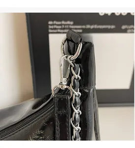 Detail of silver chain strap and metal lobster clasp on black patent leather tote bag