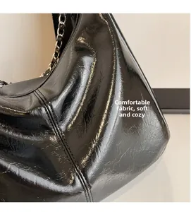 Close-up of black wrinkled patent leather texture and silver chain strap on hobo bag