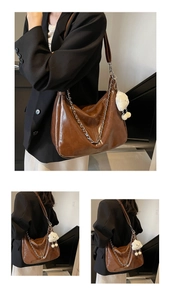 Detail of a brown glossy leather tote bag with a silver chain and white plush bear charm