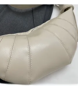 Detailed close-up of stitching and metal zipper on beige croissant crossbody bag