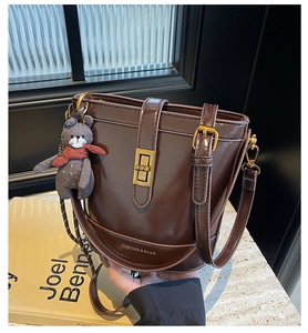 Dettaglio della borsa a secchiello in pelle marrone con chiusura dorata e orsetto