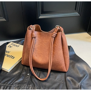 Close-up of brown leather bucket bag with unique knotted strap on dark jacket