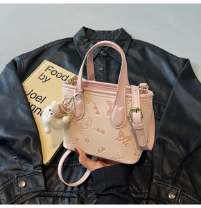 Close-up of pink embossed bucket bag with floral patterns, adjustable strap and plush charm
