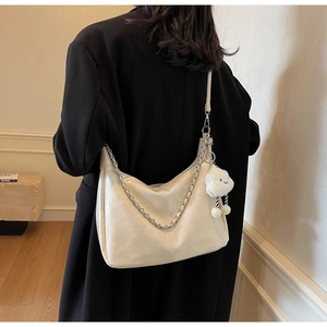Detail of cream soft leather tote bag with silver chain and white plush charm on model