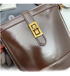 Dettaglio di una borsa a secchiello marrone scuro lucida con chiusura in metallo dorato