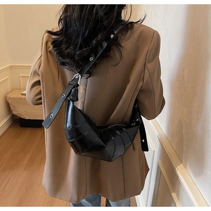Detailed view of black croissant bag in glossy leather with adjustable metal buckle strap