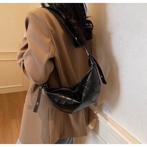 Detail of glossy black croissant shoulder bag with segmented stitching and metal buckle