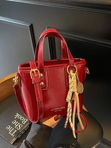 Red patent leather bucket bag with top handles and a tennis racket charm accessory