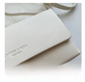 Close-up of cream crossbody bag featuring litchi texture leather and embossed logo detail