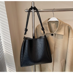 Detail of black leather tote bag featuring knot handle design and embossed branding