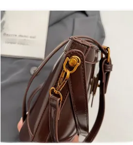 Dettaglio della fibbia dorata e pelle lucida marrone caffè su una borsa a secchiello