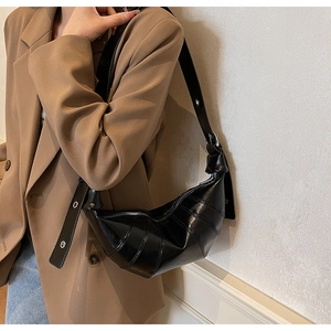 Detail of black leather croissant bag with wide shoulder strap worn over a brown blazer