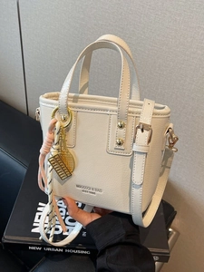 Chic cream leather bucket bag with gold hardware and unique mini charms on the handle