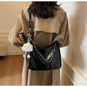 Close-up of black patent leather hobo bag with silver chain and plush cloud pendant charm