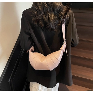 Detailed view of glossy pink leather croissant bag shown on person in black suit