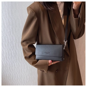 Detail of a black matte leather flap bag worn with a brown vintage blazer over the shoulder