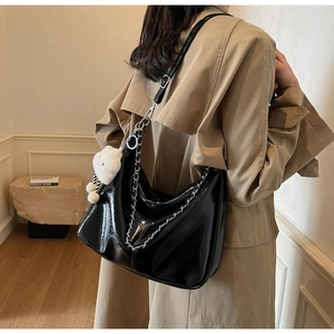 Detail of black glossy tote bag with silver chain and white plush ball on a model