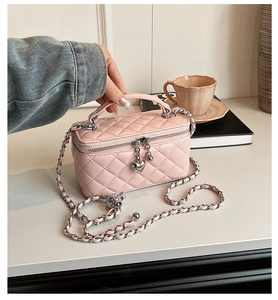 Pink quilted box bag with silver chain strap and heart charm detail on table