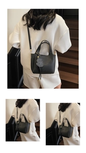 Detail of black lychee leather bucket bag with top handles and a cute dog charm