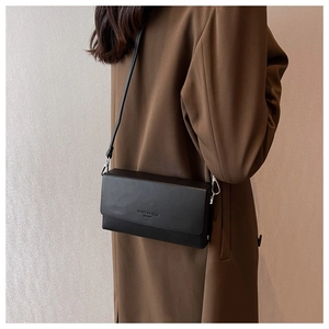 Detail of matte black leather crossbody bag with embossed lettering on brown coat