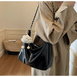 Close-up of black patent leather hobo bag with gold chain strap and plush white charm