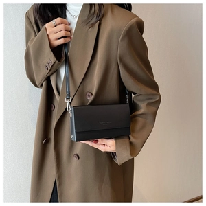 Detail of black leather crossbody bag with silver buckle worn on a brown blazer coat