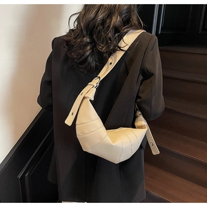 Detail of cream croissant bag with pleated design worn over a black blazer on shoulder