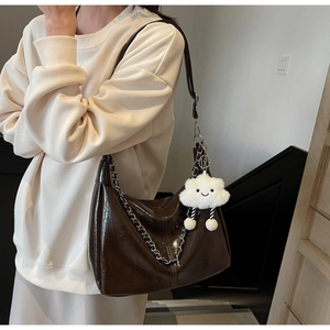 Detail of dark brown glossy tote bag with silver chain and white cloud charm
