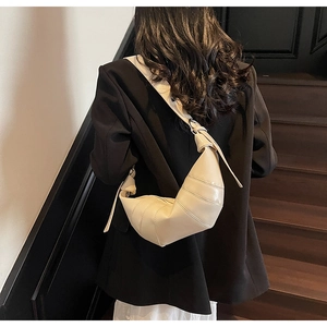 Detail view of a beige croissant bag featuring pleats and wide shoulder strap on a model