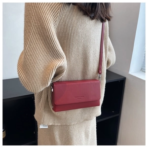 Detail of dark red leather crossbody bag with silver hardware on beige knit outfit
