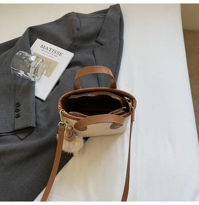 Top view of two-tone cream and brown mini bucket bag with plush charm on a white surface