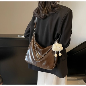 Detail of dark brown glossy leather tote bag with silver chain and white plush charm