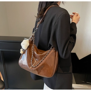 Brown patent leather tote bag detail with silver chain and plush bear charm on model