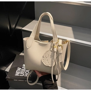 Detail of cream white pebbled leather bucket bag with dog charm and gold hardware