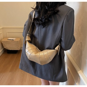 Modern beige pleated croissant bag worn by a model in a minimalist interior setting