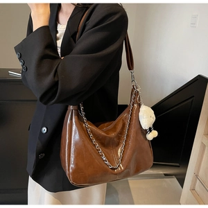Close-up of brown glossy hobo bag with silver chain and white plush lamb charm accessory