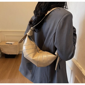 Detail view of beige croissant bag with pleated stitching texture and metal zipper closure