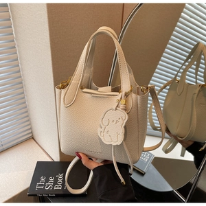 Detail view of beige textured leather bucket bag with cute puppy charm and mirror reflection