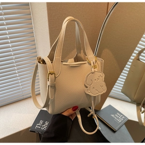 Detail showing creamy off-white lychee texture leather bucket bag with dog charm
