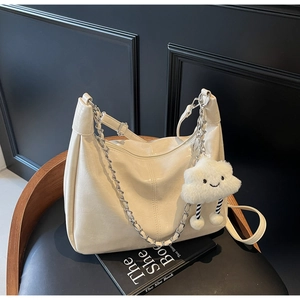 Detail of creamy white leather tote with plush cloud charm and metal chain on a black chair