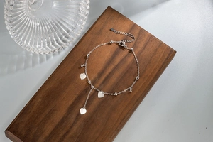 Detail of silver heart tassel anklet with polished beads on premium wooden stand