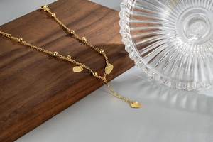 Detail of gold beaded anklet featuring heart charms on a minimalist metal chain link