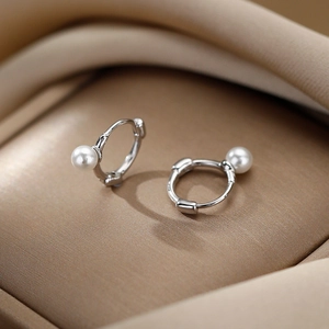 Élégantes créoles en argent avec perles blanches sur un fond minimaliste en soie dorée