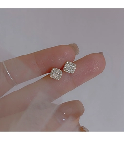 Close-up of hand holding geometric gold earrings with micro-paved white zircon stones